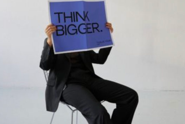 Woman holding a “think bigger” sign representing creative advertising and digital marketing strategy.