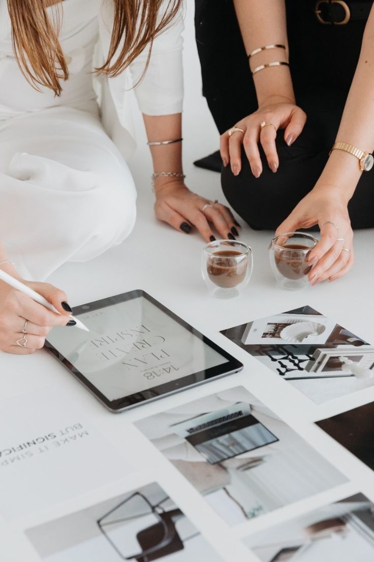 Two women collaborating on custom logo design in Newcastle, drawing on an iPad with branding images spread across a table.