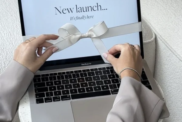 Woman untying a bow around a MacBook with "New Launch" on the screen, representing website redesign and new website launch.