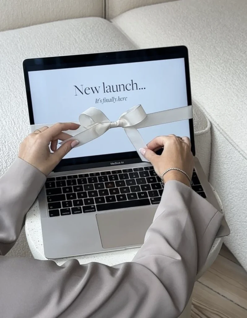 Our Blog Woman untying a bow around a MacBook with "New Launch" on the screen, representing website redesign and new website launch.